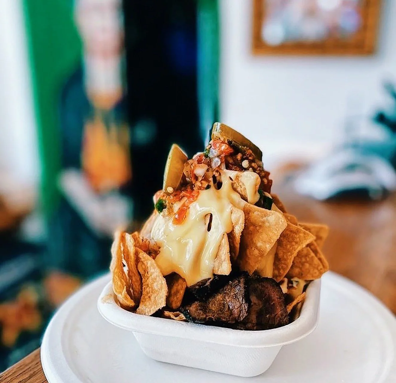 A serving of loaded nachos with chips, melted cheese, jalapeños, ground beef, salsa, and sour cream in a white bowl.