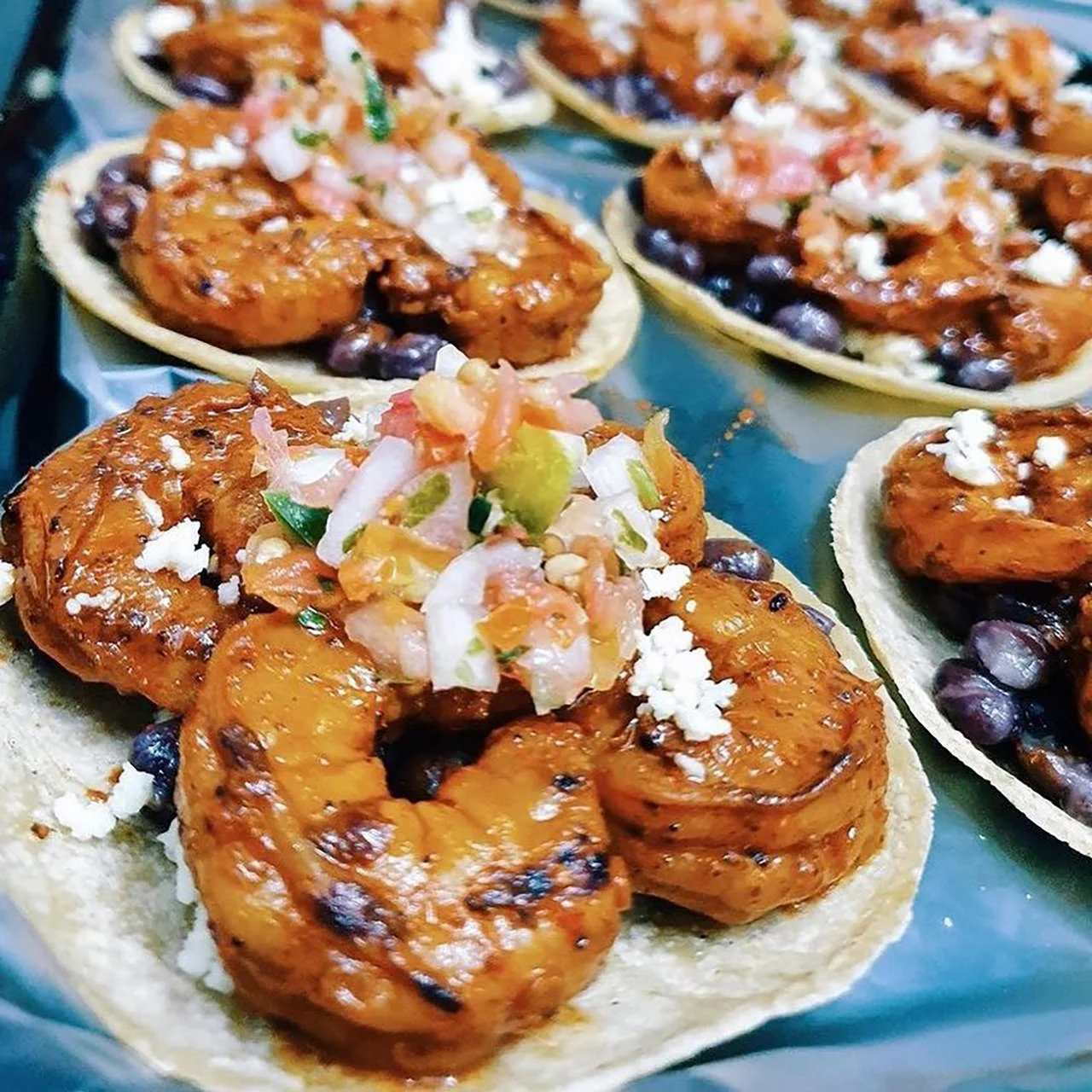 Close-up of shrimp tostadas topped with salsa, crumbled cheese, and diced vegetables on small tortillas.