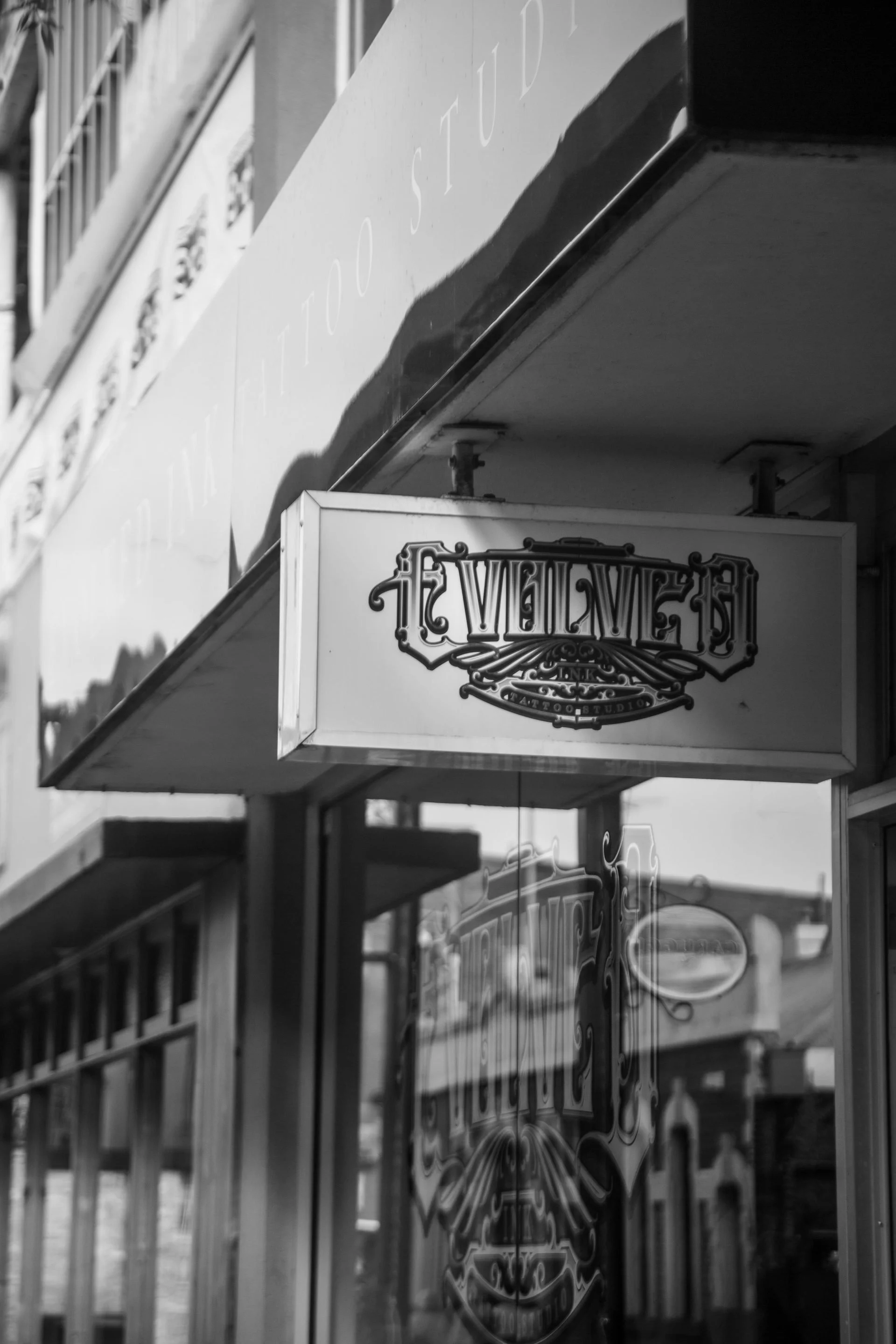 The photo shows the entrance sign of a tattoo studio with the name 'Heavilves' in ornate lettering, mounted on a building with reflective glass windows.