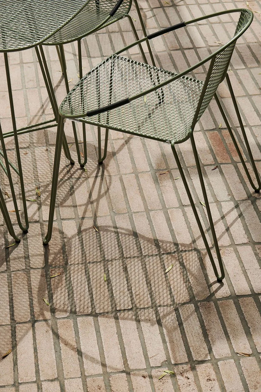 Metal outdoor table and chair on brick patio with shadows casting on the ground.
