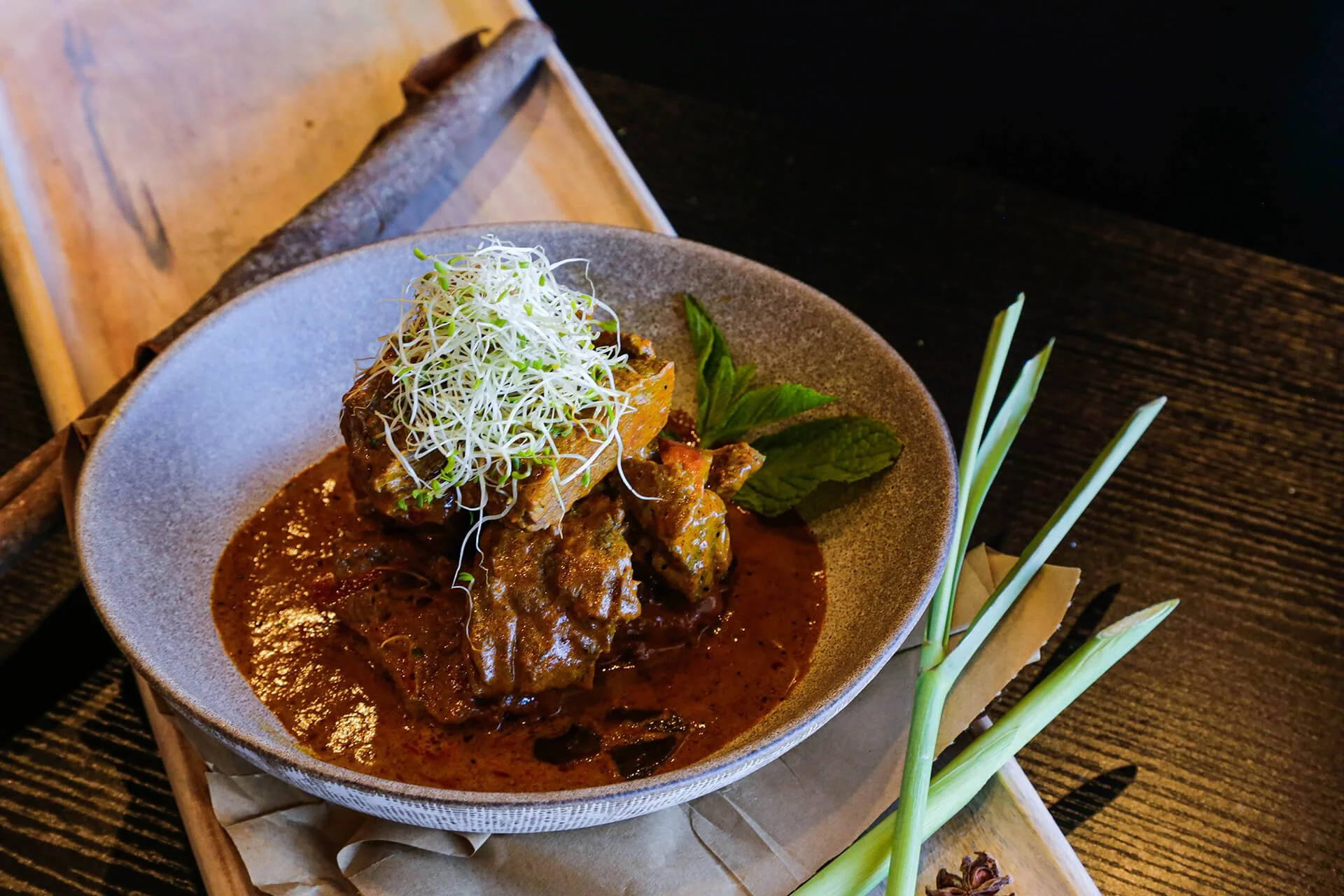 A bowl of spicy beef curry garnished with fresh herbs and microgreens, served with green onions on the side.