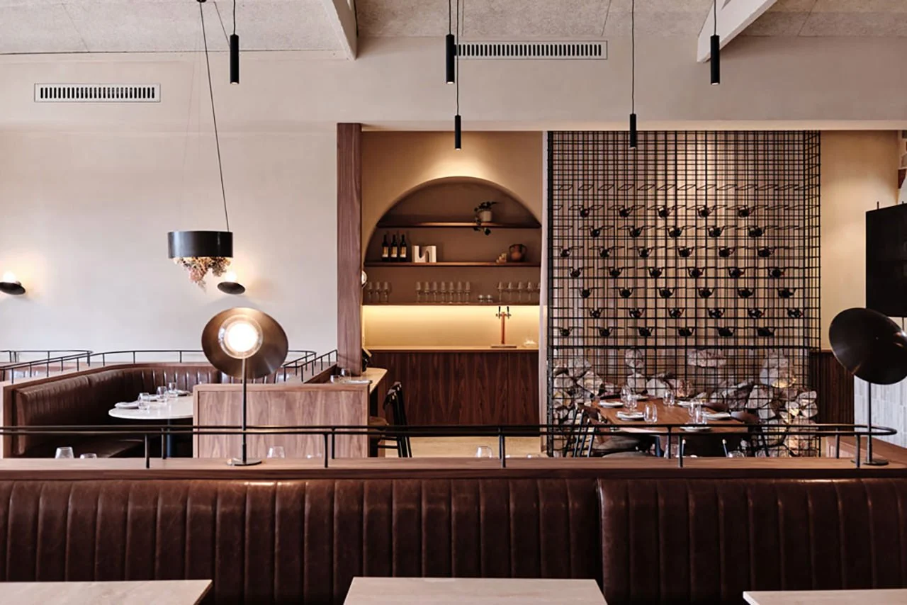 Interior of a modern restaurant with wooden and leather furnishings, decorative wall art, and ambient lighting.
