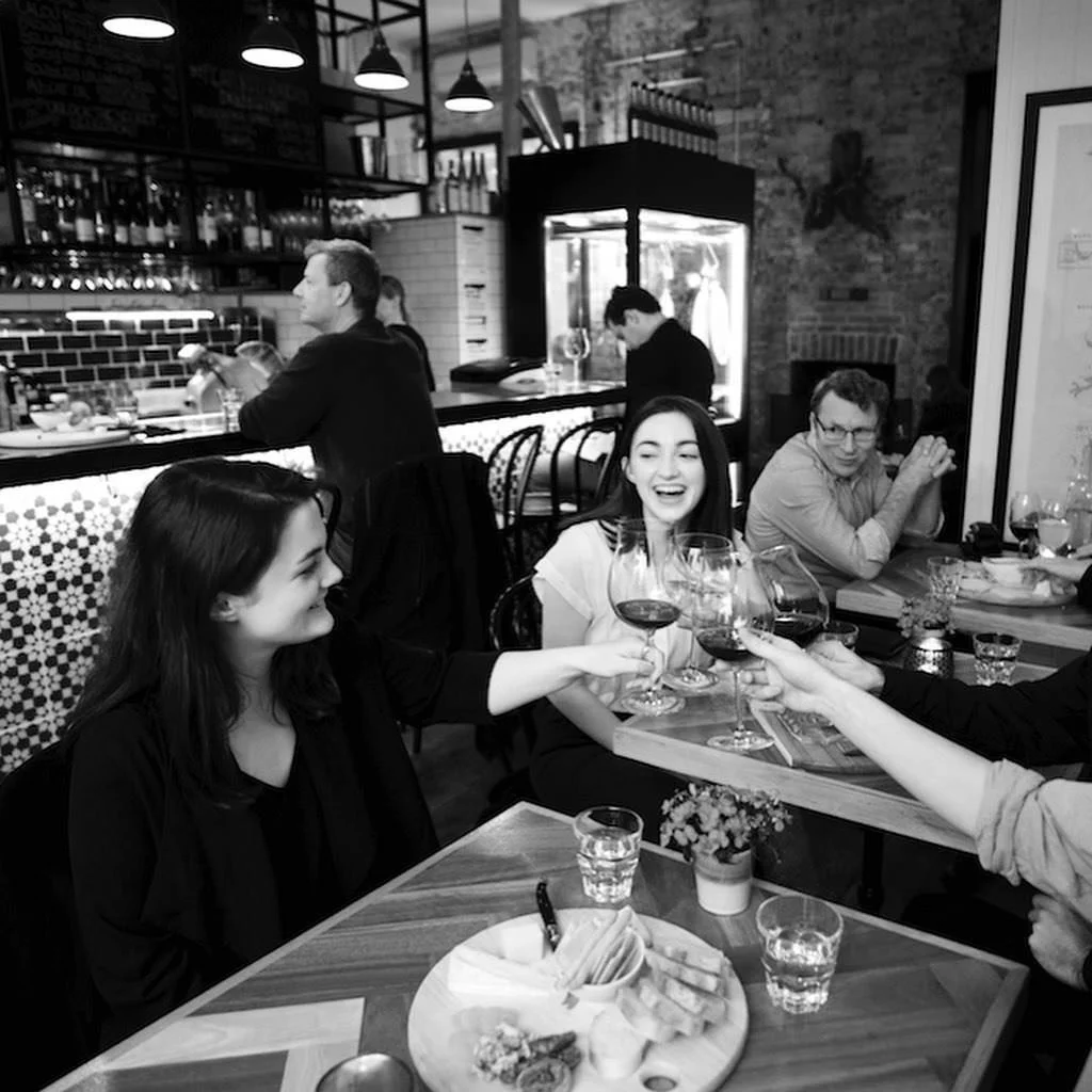 People sitting around a table in a restaurant, toasting with wine glasses, smiling and enjoying their time.