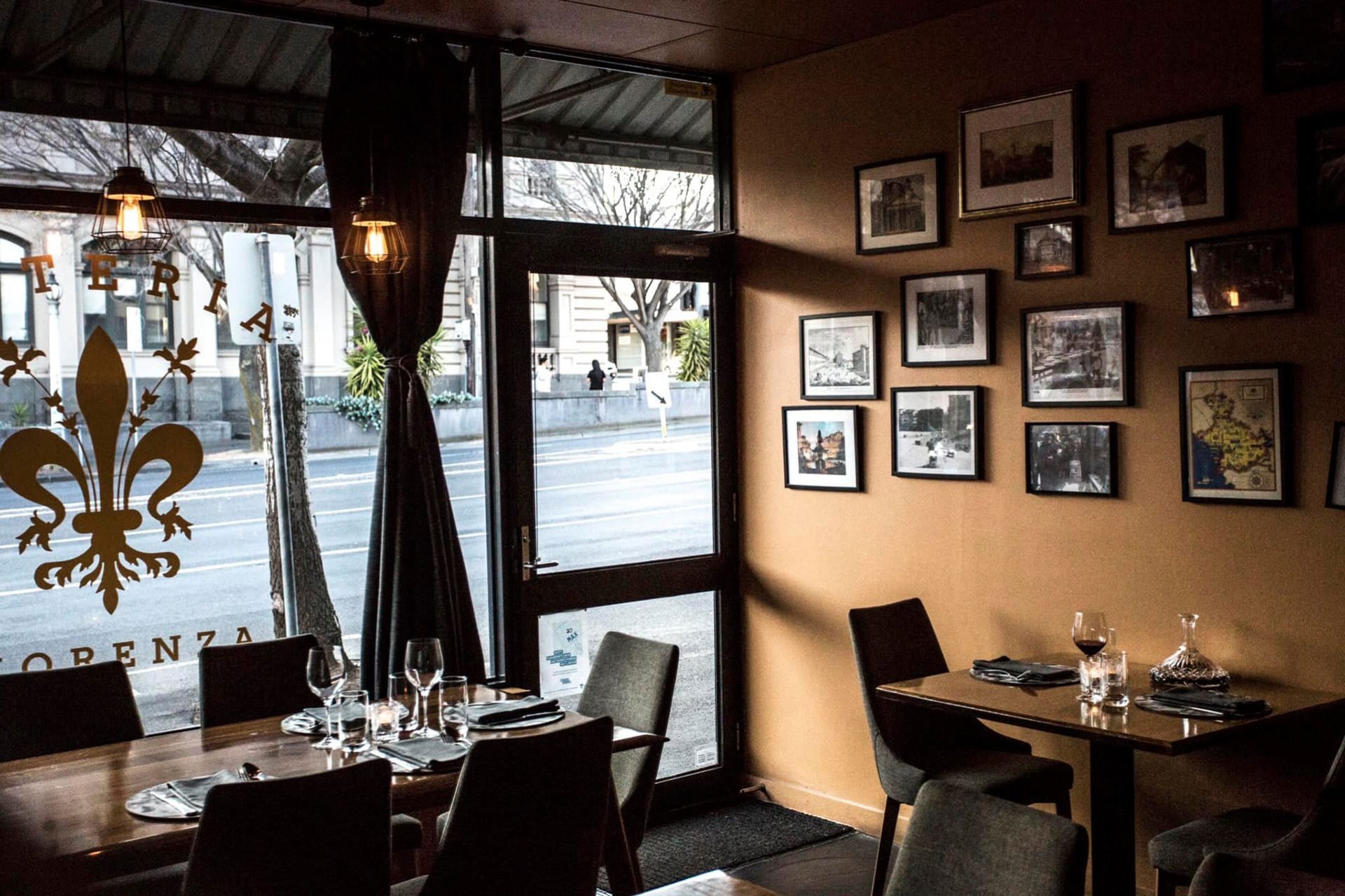 Interior of a restaurant with tables set for dining, framed photos on the wall, and large windows letting in natural light.