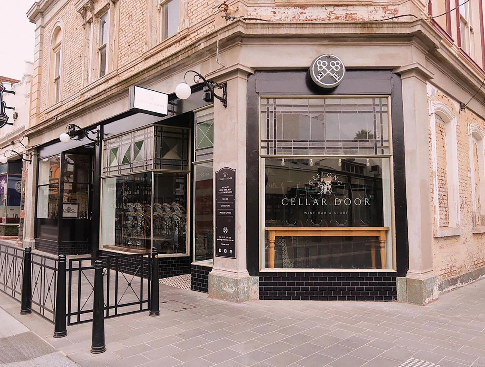 Corner view of a wine bar and store named 'Cellar Door' with large windows, sign, and outdoor patio area with metal railings.