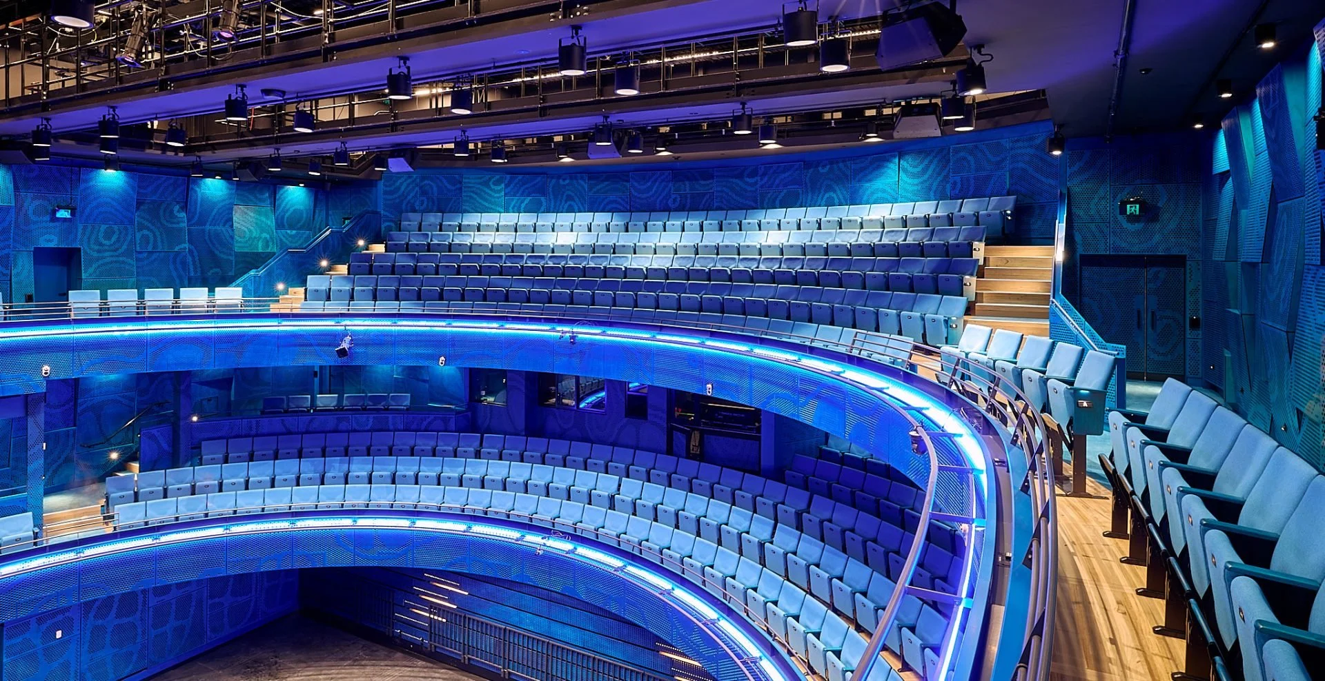 Multiple tiers of blue seats in a modern auditorium or theater with blue lighting accents.