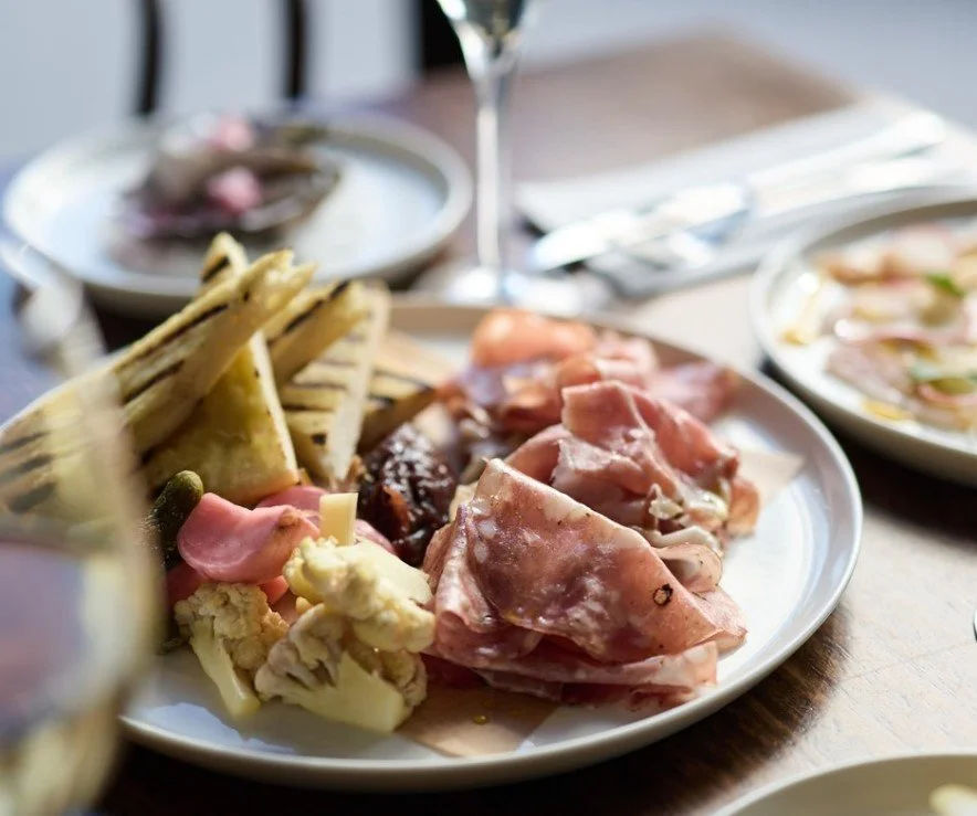 A plate of assorted cold cuts, cheeses, and grilled bread with some vegetables, on a dining table at a restaurant.