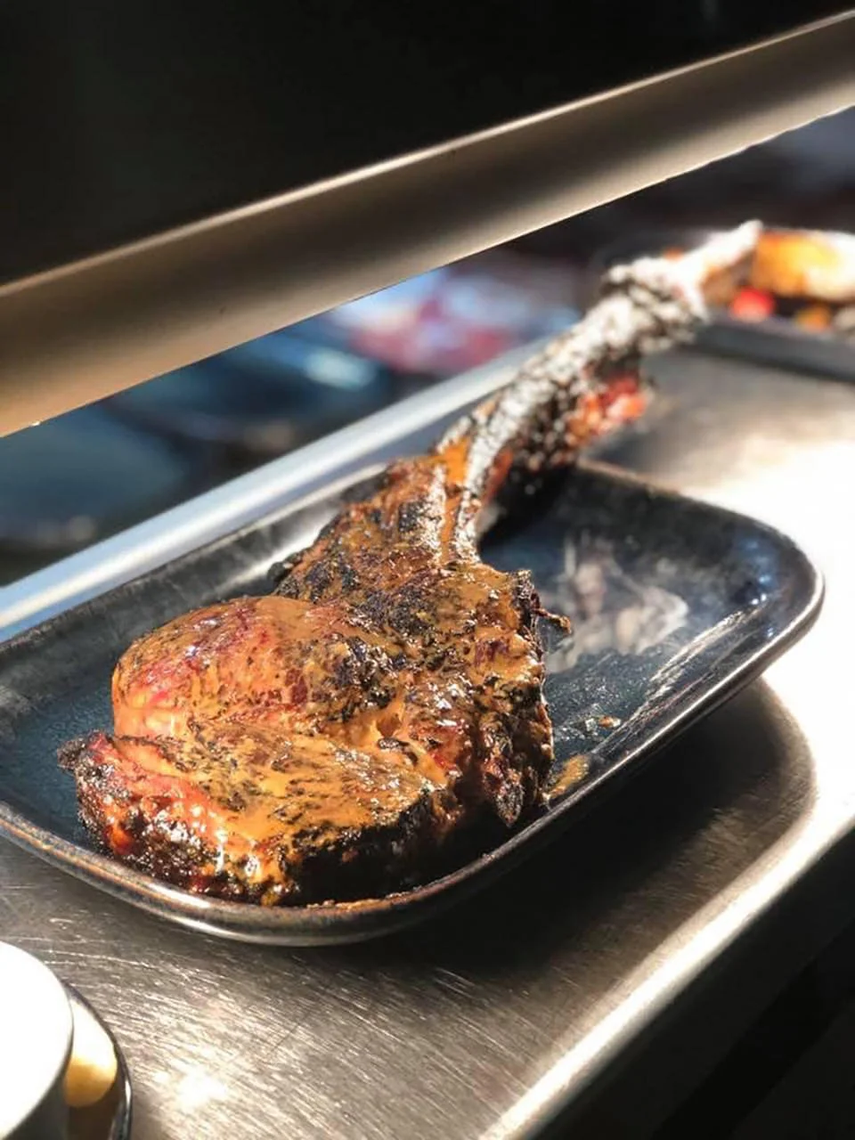 A cooked beef steak in a metal tray, situated under a heat lamp in a professional kitchen.