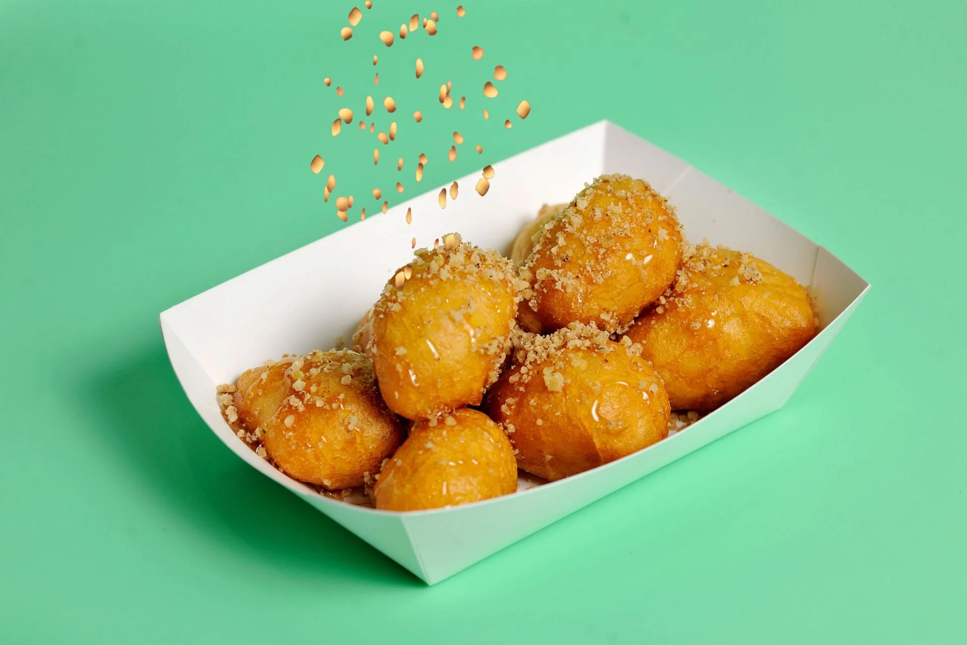 Fried cheese balls in a white paper tray, sprinkled with breadcrumbs, against a light green background.