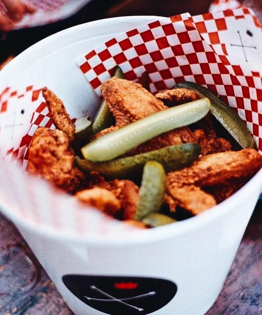 Fried chicken tenders with pickle slices in a white basket lined with red and white checkered paper.