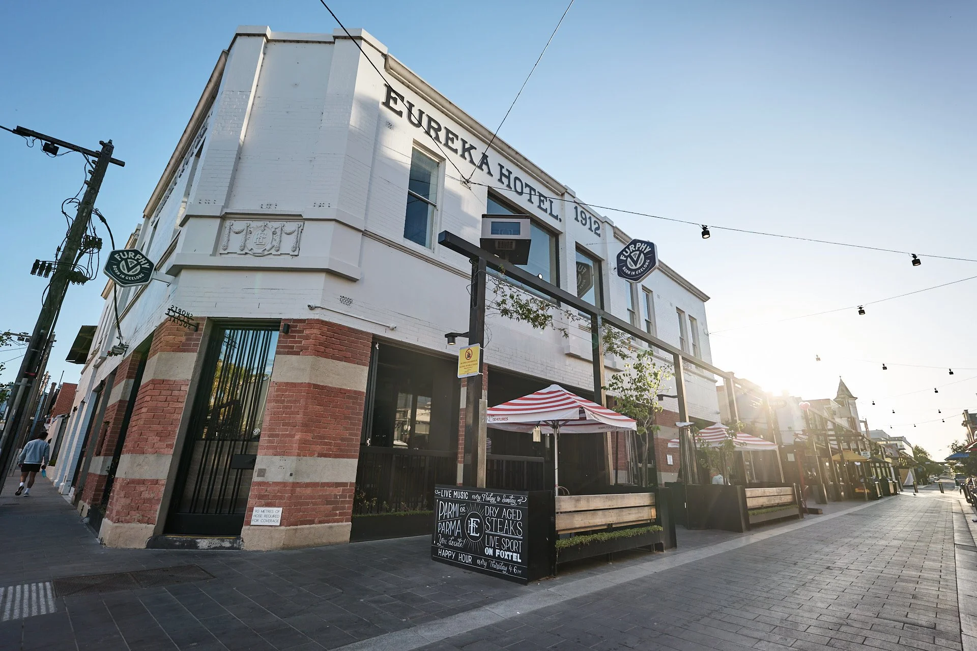 Street view of Eureka Hotel, a historic building from 1912, with outdoor seating and striped umbrellas, illuminated by the setting sun.