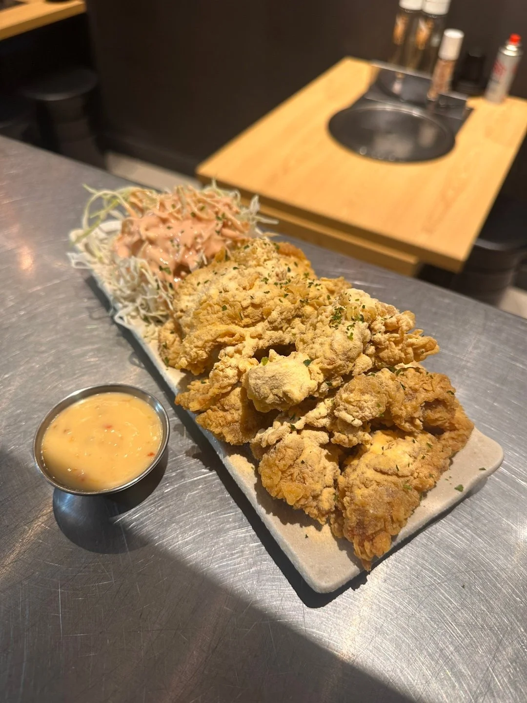 A rectangular plate with fried chicken pieces, shredded cabbage salad with sauce, and a small cup of dipping sauce, on a metal table.