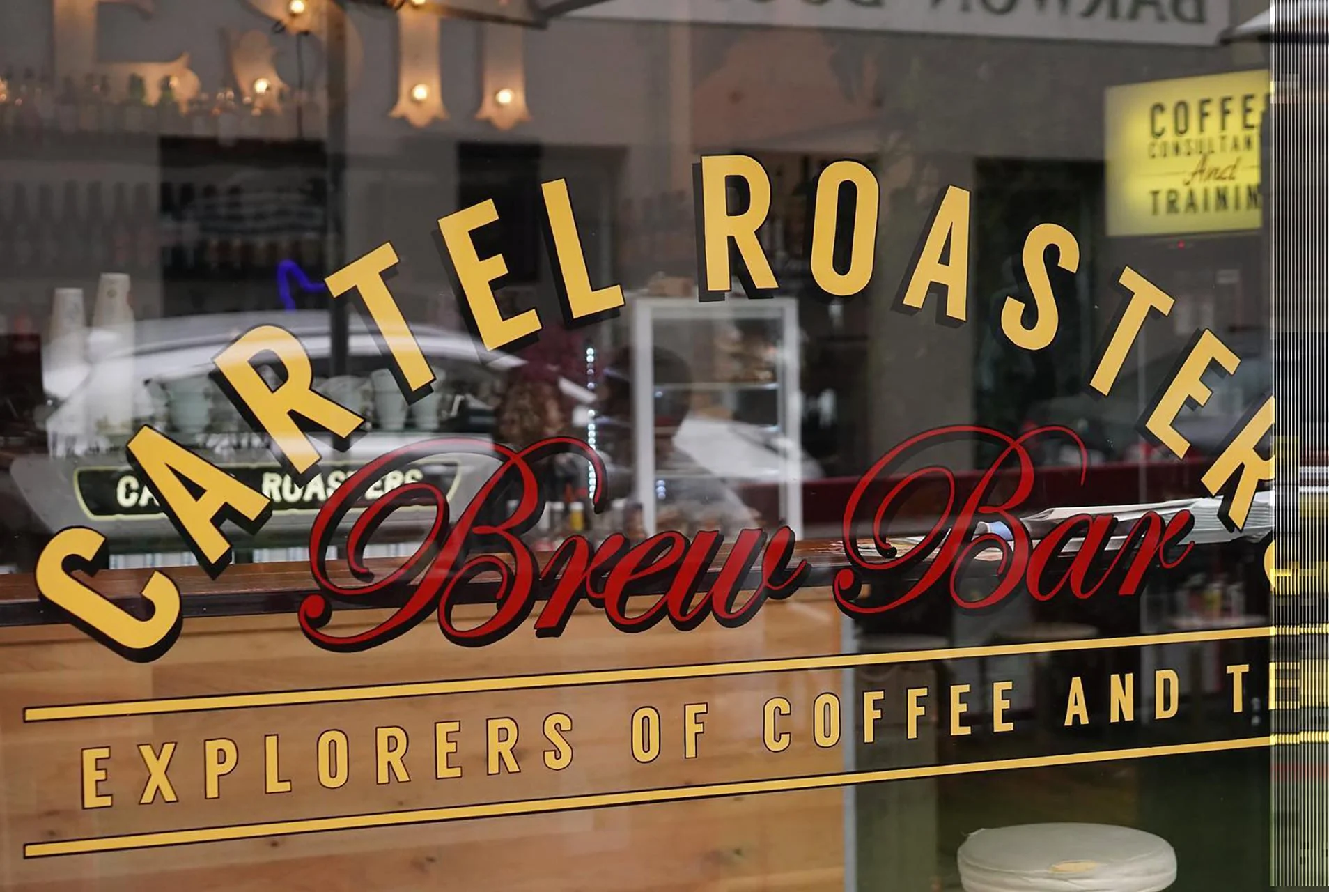 Decorative window sign for Calretel Roaster Brew Bar, featuring the slogan 'Explorers of Coffee and T' with colorful text and a reflection of the street scene inside the cafe.
