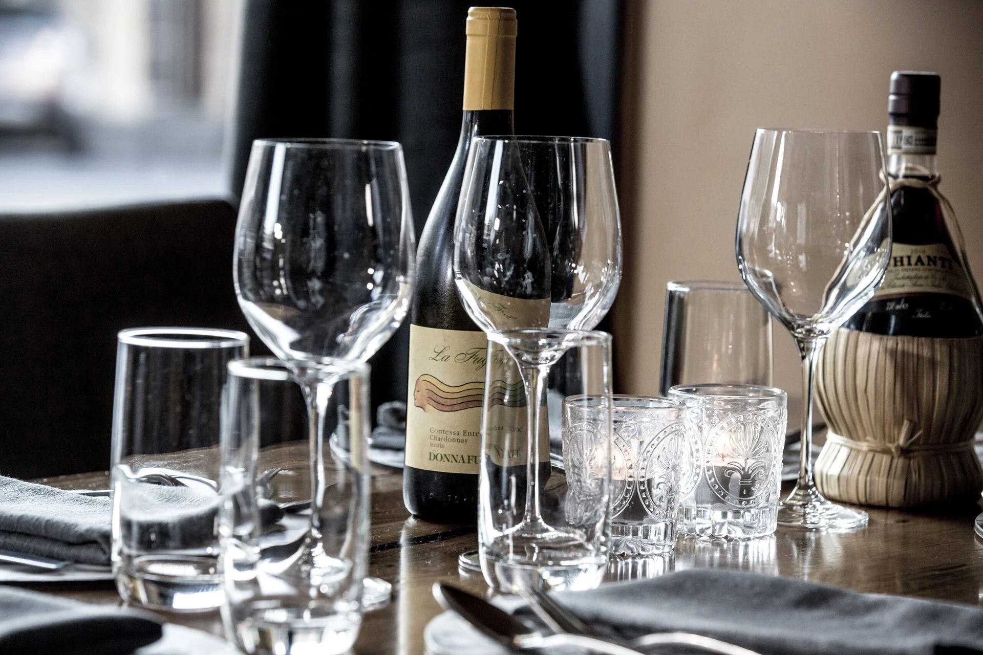A table set for drinking with multiple wine glasses, a bottle of wine, a water bottle, and drinking glasses, with napkins and utensils.