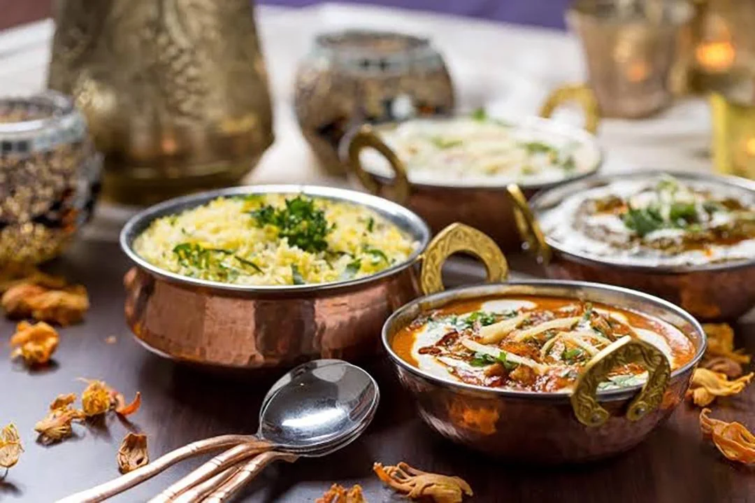 Variety of Indian dishes in traditional copper bowls on a wooden table.