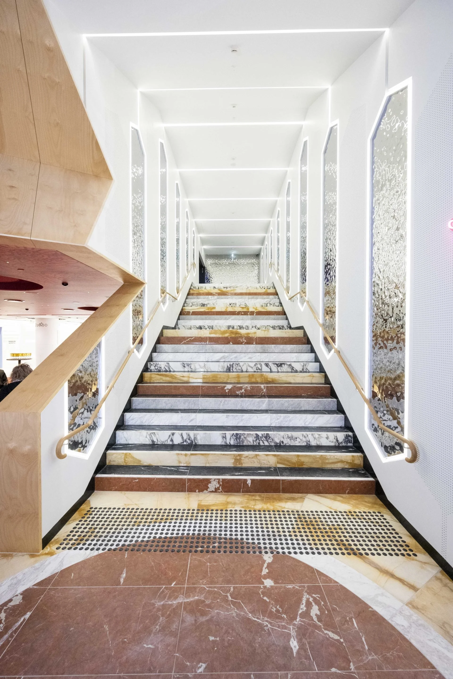 Marble staircase with modern white walls and gold accents, leading upwards in a well-lit interior space.