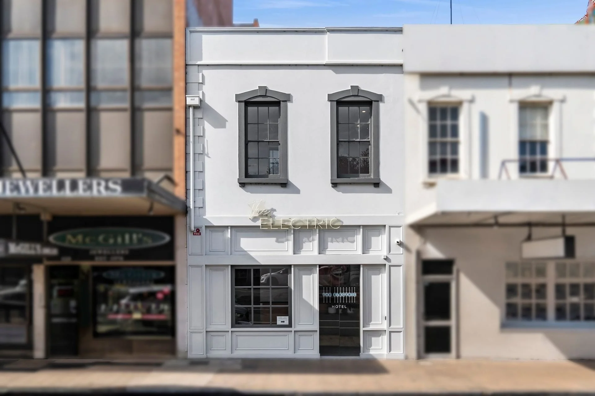White two-story building with black window frames and a neon sign that reads "The Electric" on the front.