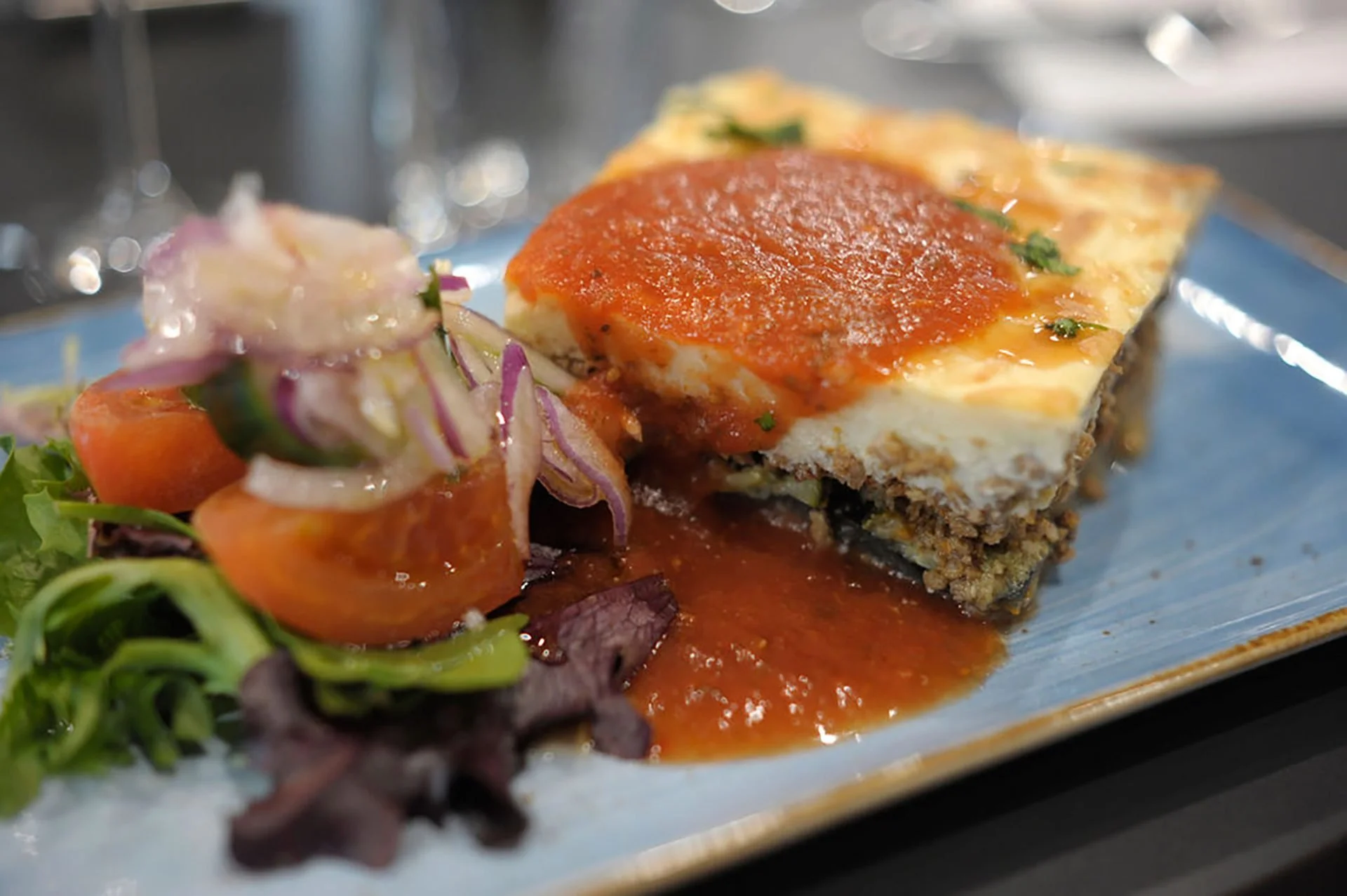 Slice of baked casserole topped with tomato sauce served with a side salad of chopped vegetables and greens