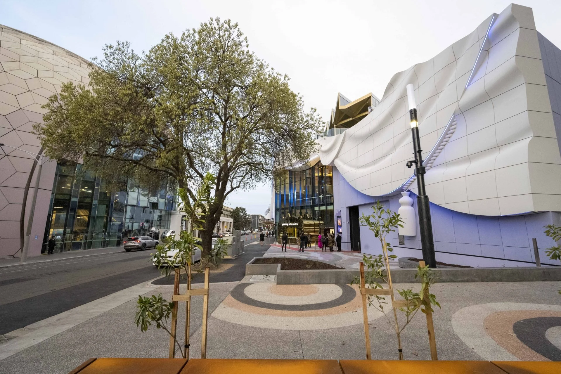 Modern urban scene with unique architectural buildings, a tree, sidewalk, and pedestrians