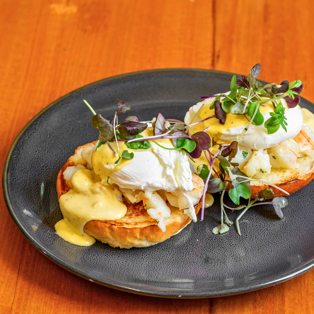 Poached eggs over toasted bread with microgreens and hollandaise sauce on a black plate.