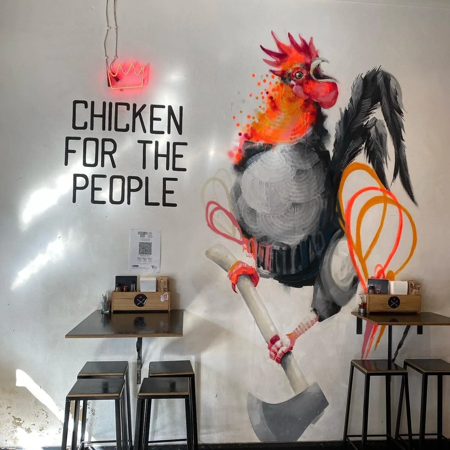 Interior wall mural featuring a colorful chicken with a punk hairstyle, holding an axe, with the phrase "Chicken for the People" and a neon crown sign.