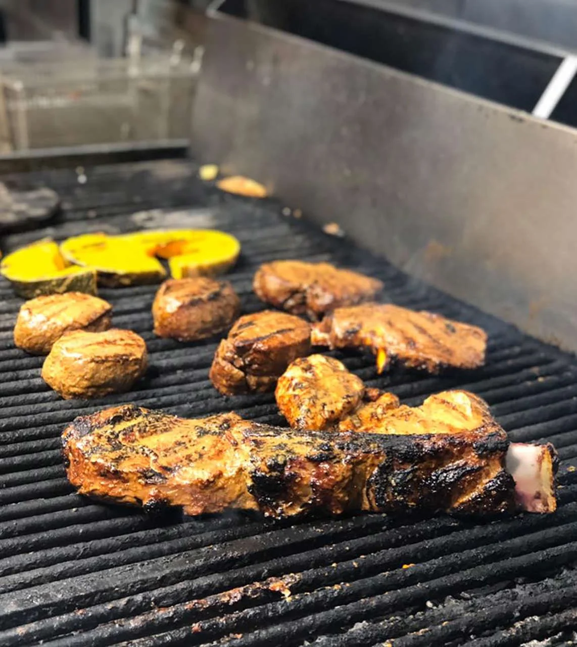 Grilled meat, squash, and onions cooking on a BBQ grill.