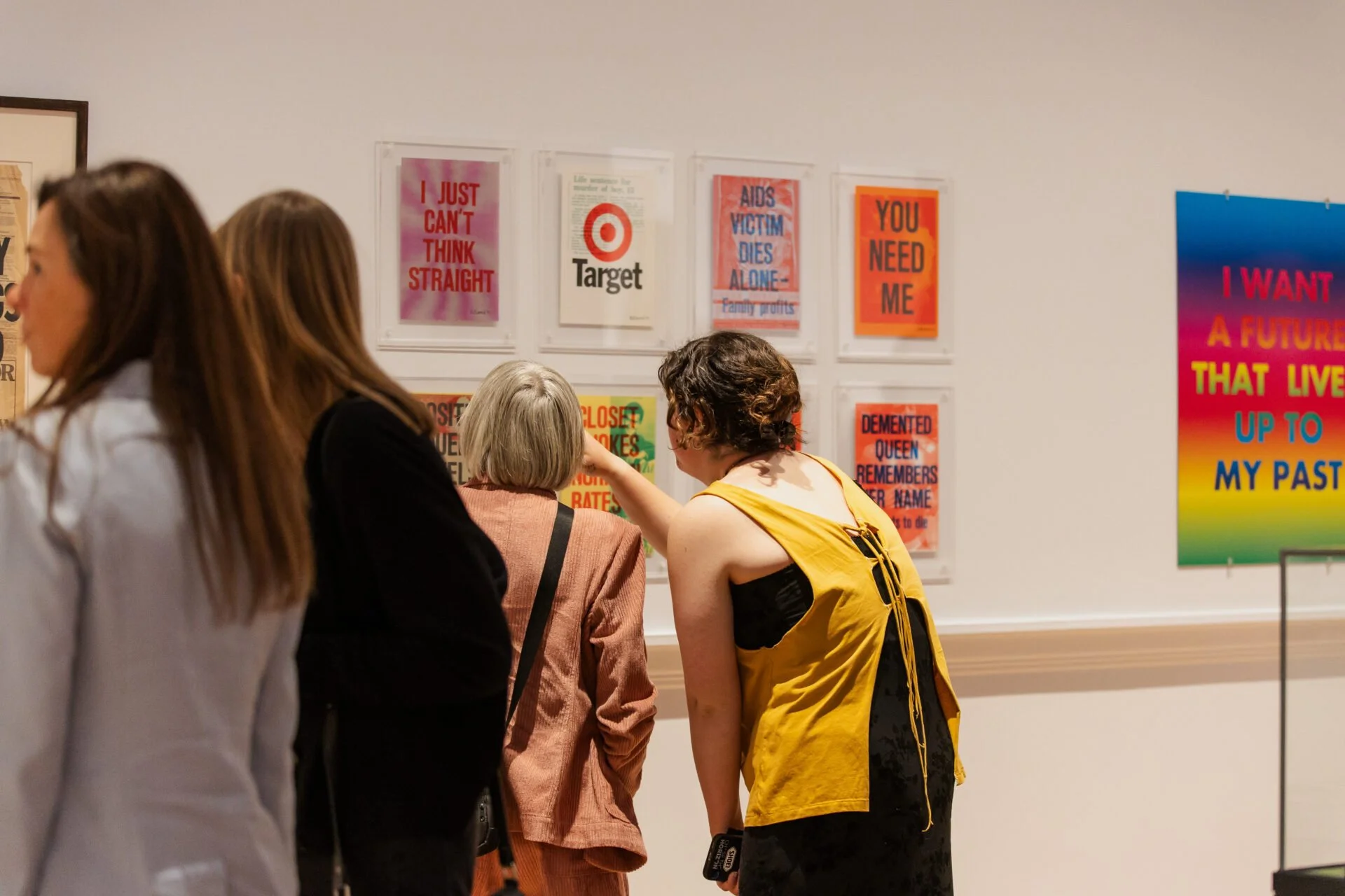 People viewing colorful posters on a gallery wall, with titles on issues like targets, AIDS, and social justice.