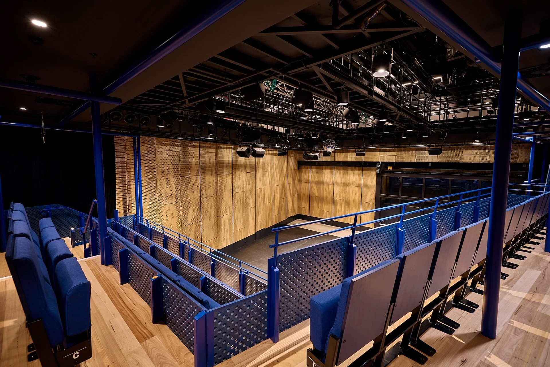 Empty auditorium with tiered seating, a stage at the front, and wooden walls.