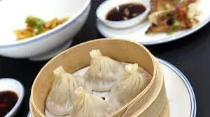 Dim sum dumplings in a bamboo steamer with dipping sauces in the background.