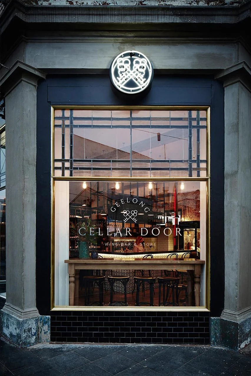 Outside view of a restaurant or bar named 'Cellar Door' with large window and a neon sign of crossed keys above the entrance.
