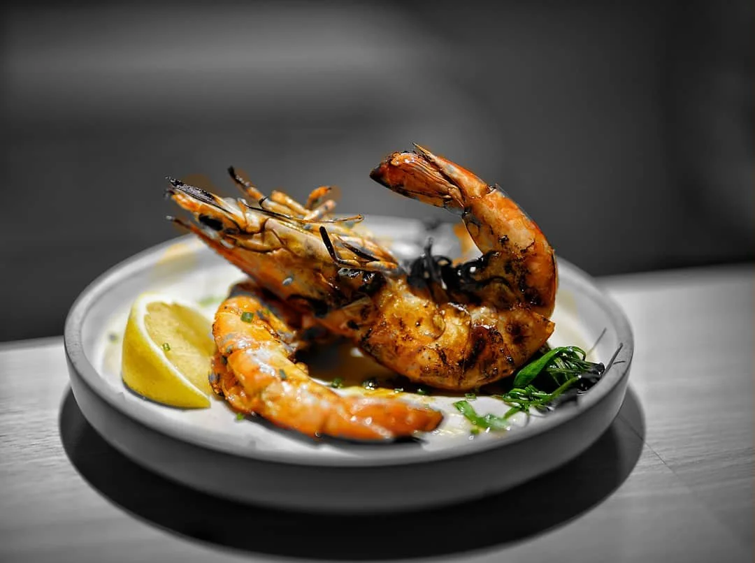 Grilled shrimp served with lemon wedges and green herbs on a white plate.