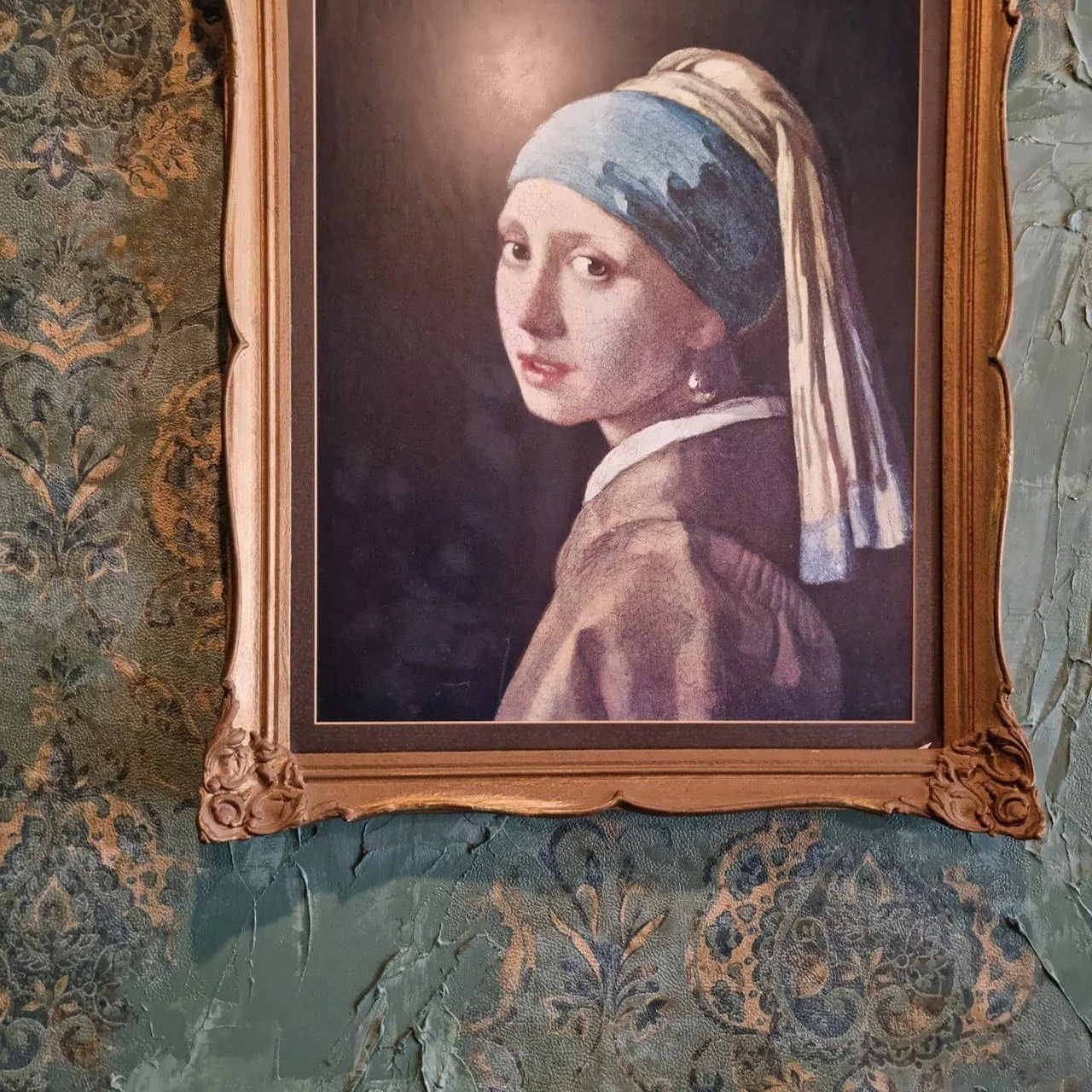 A framed portrait of a woman with a headscarf, painted in a classical style, hanging on a vintage, patterned green wall.