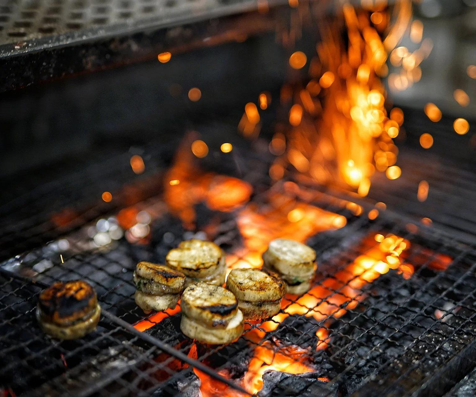 Small grilled meat sliders on a grill with orange flames and sparks.