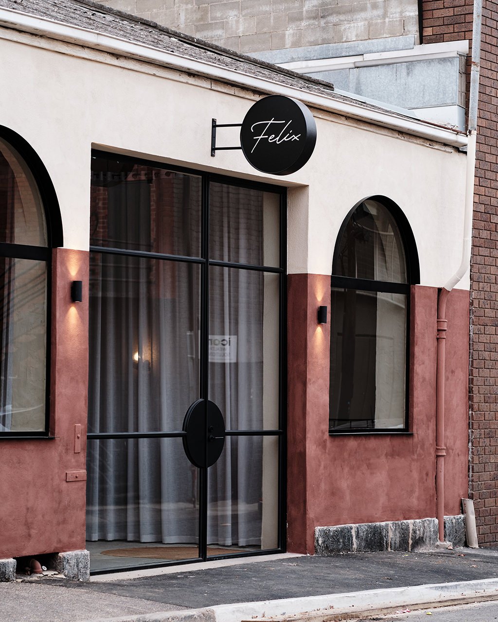 Exterior of a modern building with a rounded black sign that says 'Félix' above a glass door, accompanied by large arched windows and warm wall-mounted lights.