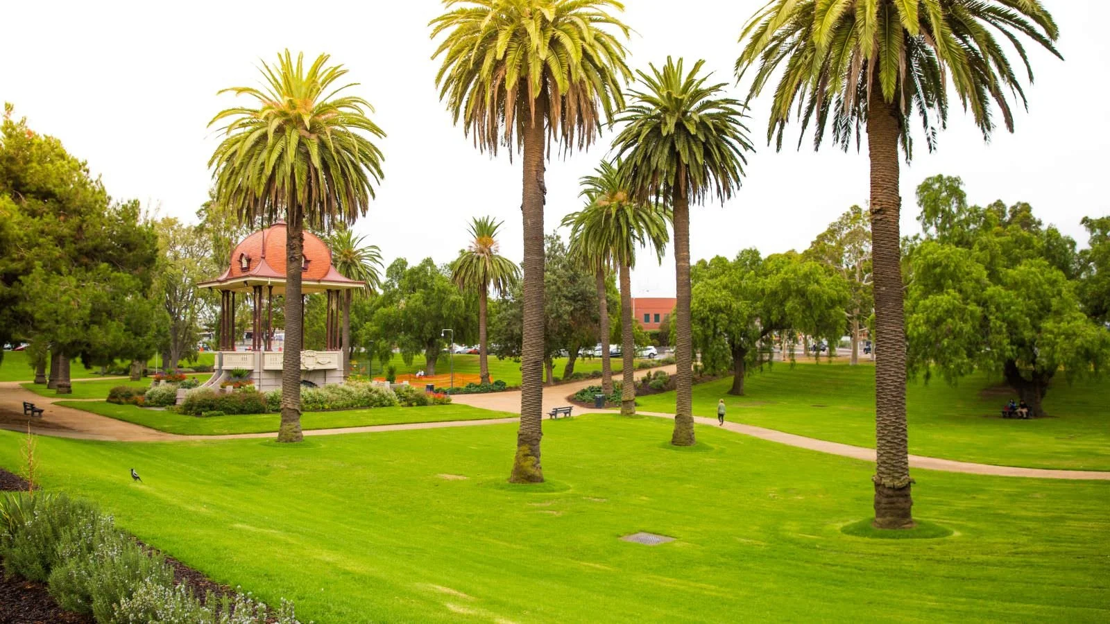 A park with palm trees, a gazebo, walking paths, benches, and greenery.