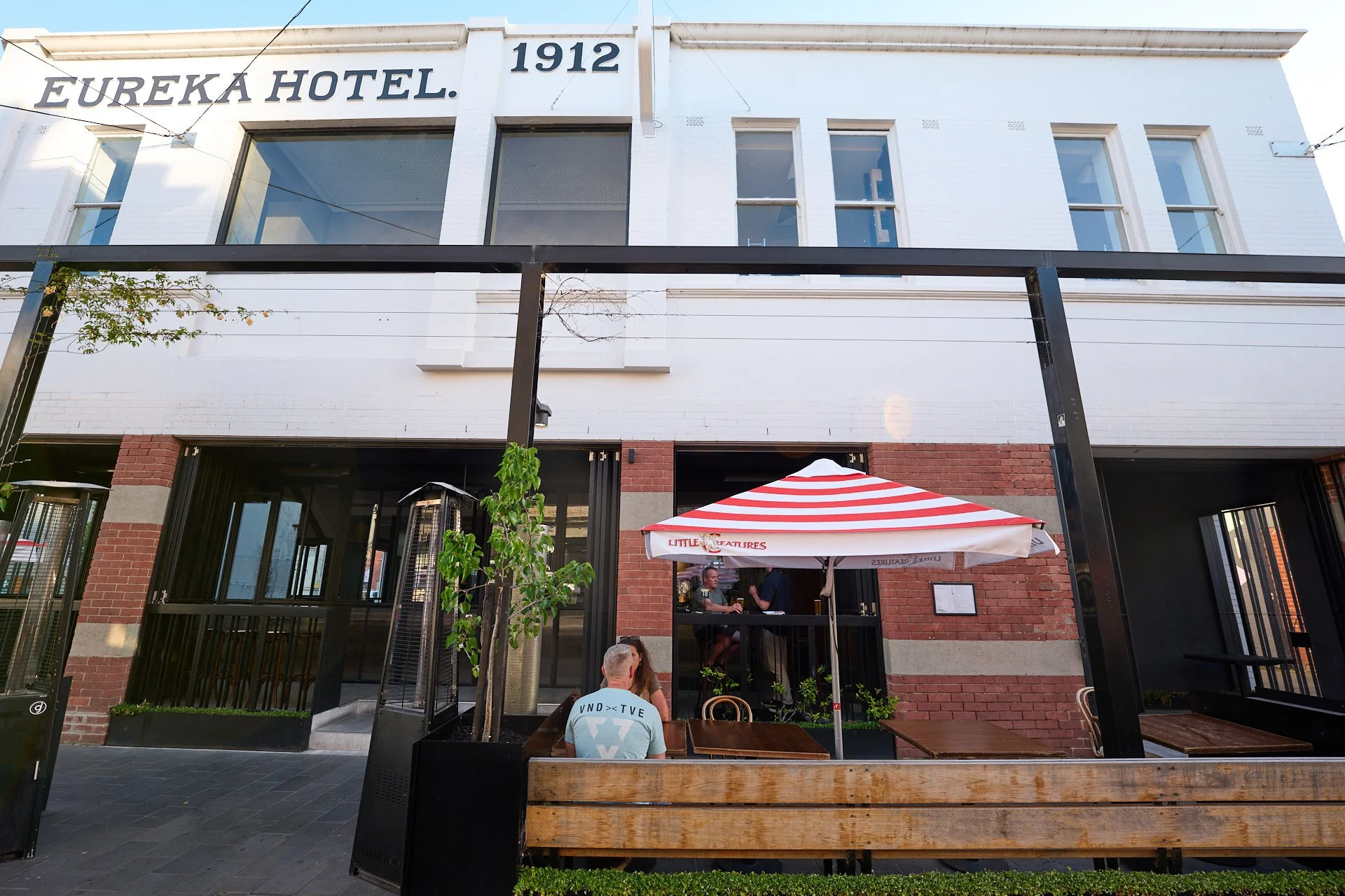 Street view of Eureka Hotel building with outdoor seating area, a red and white striped umbrella, and patrons sitting outside