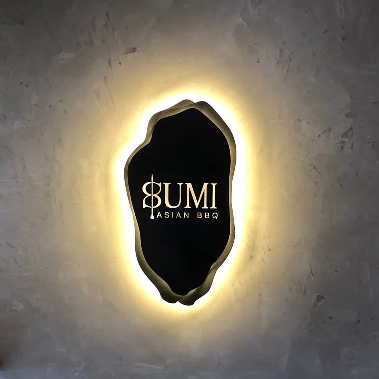 Backlit sign for Bumi Asian BBQ with a black background and white text, decorative shape around the sign.