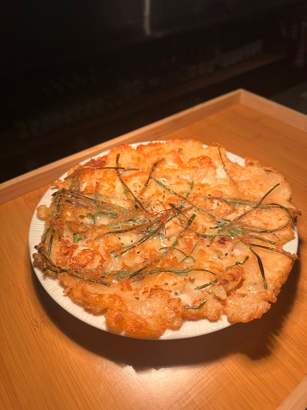 A crispy, golden-brown seafood pancake topped with green chives on a white plate.