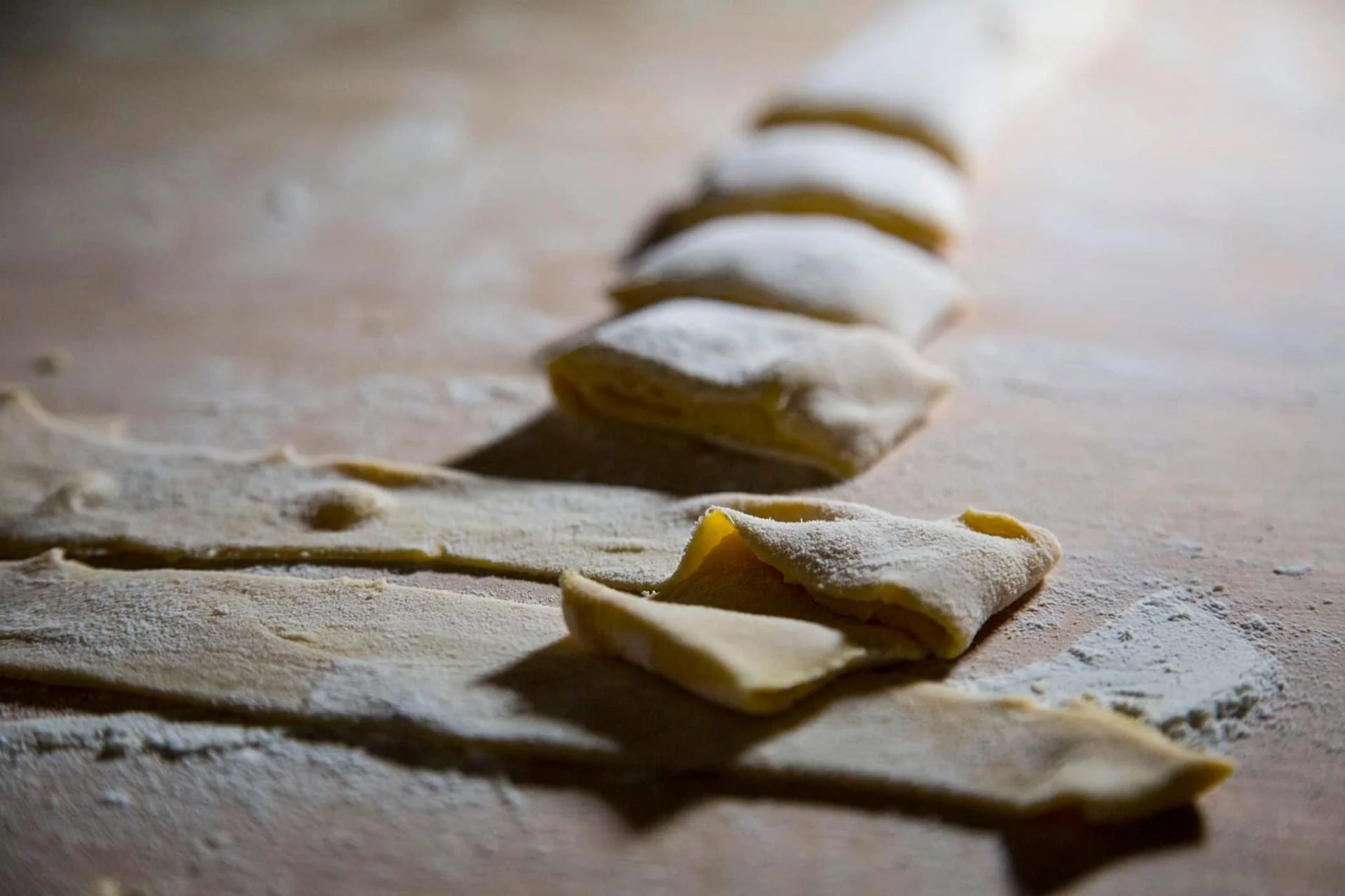 Uncooked homemade pasta pieces arranged in a line on a floured wooden surface.