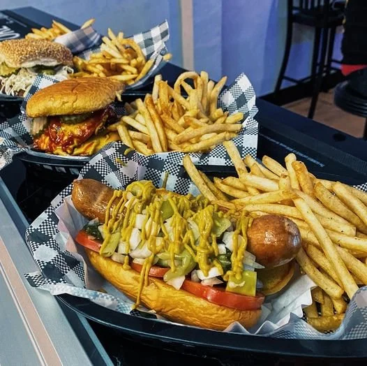 Three baskets of food containing sandwiches, fries, and hotdogs on a counter at a restaurant.