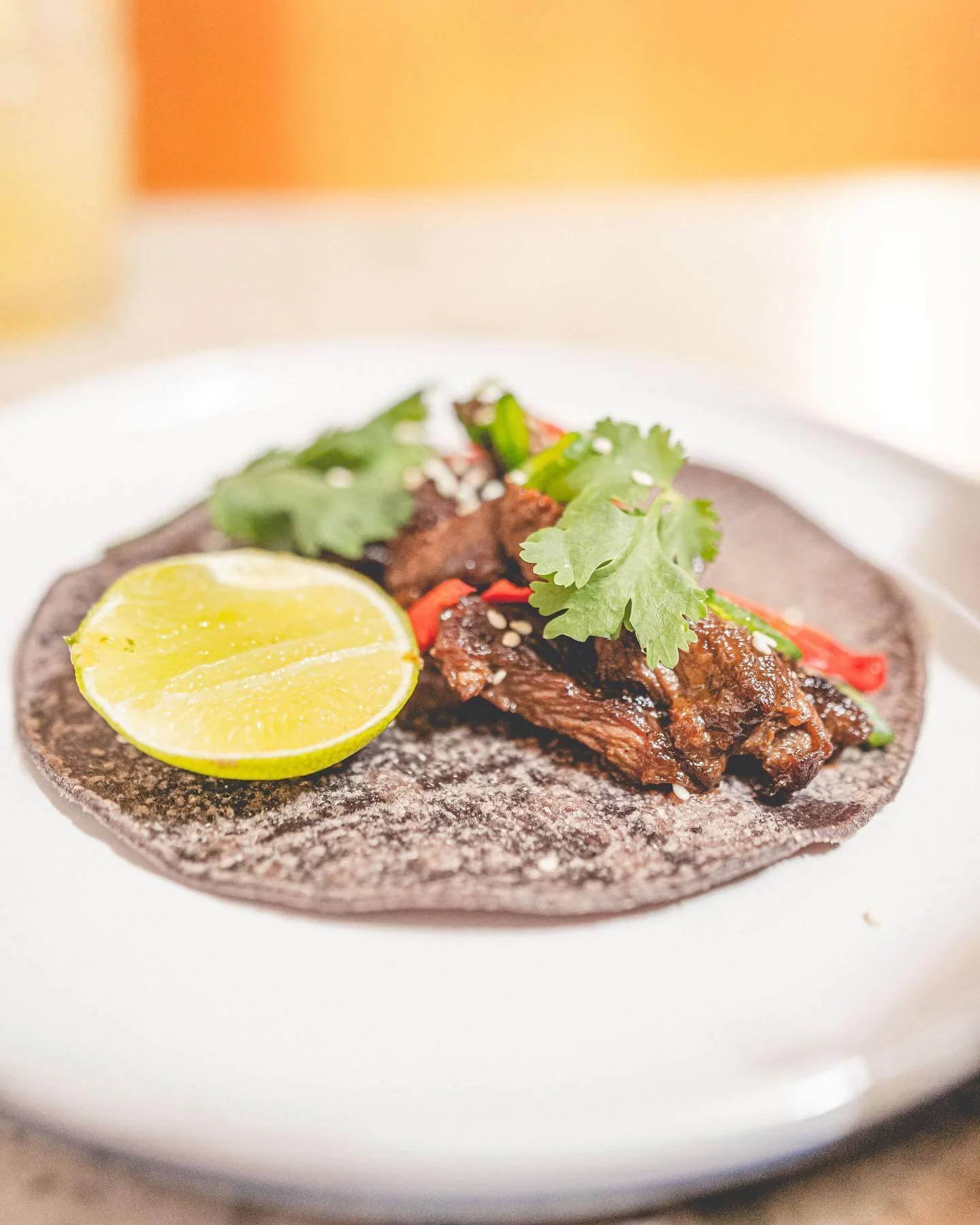 Lime wedge, cooked beef, cilantro, and red chili on a blue corn tortilla