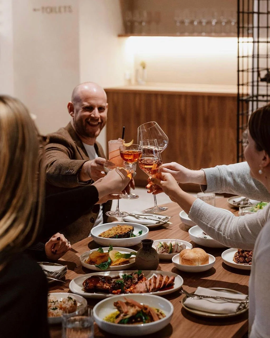 A group of friends enjoying a meal together at a restaurant, raising glasses in a toast with various dishes on the table.