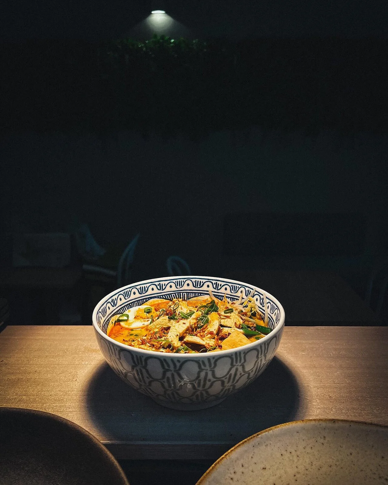 Bowl of spicy Asian noodle soup garnished with green onions on a wooden surface with dark background.