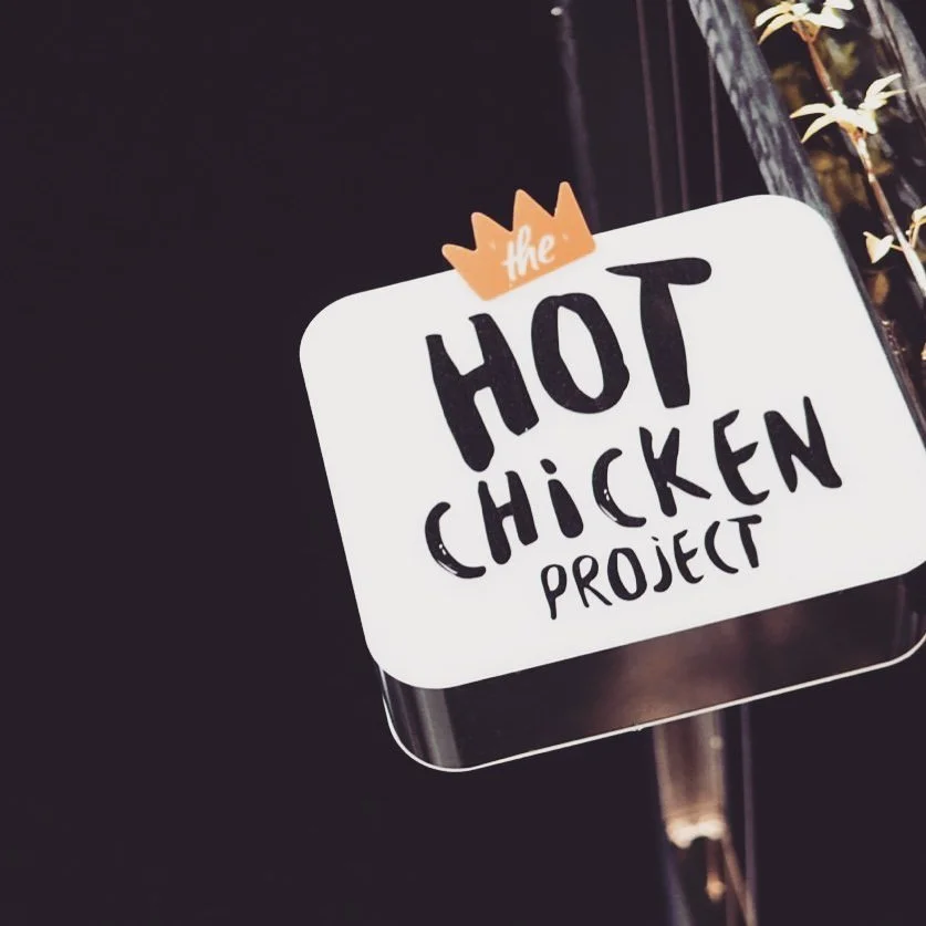 Sign reading 'The Hot Chicken Project' with a small crown above the word 'the,' against a dark background.