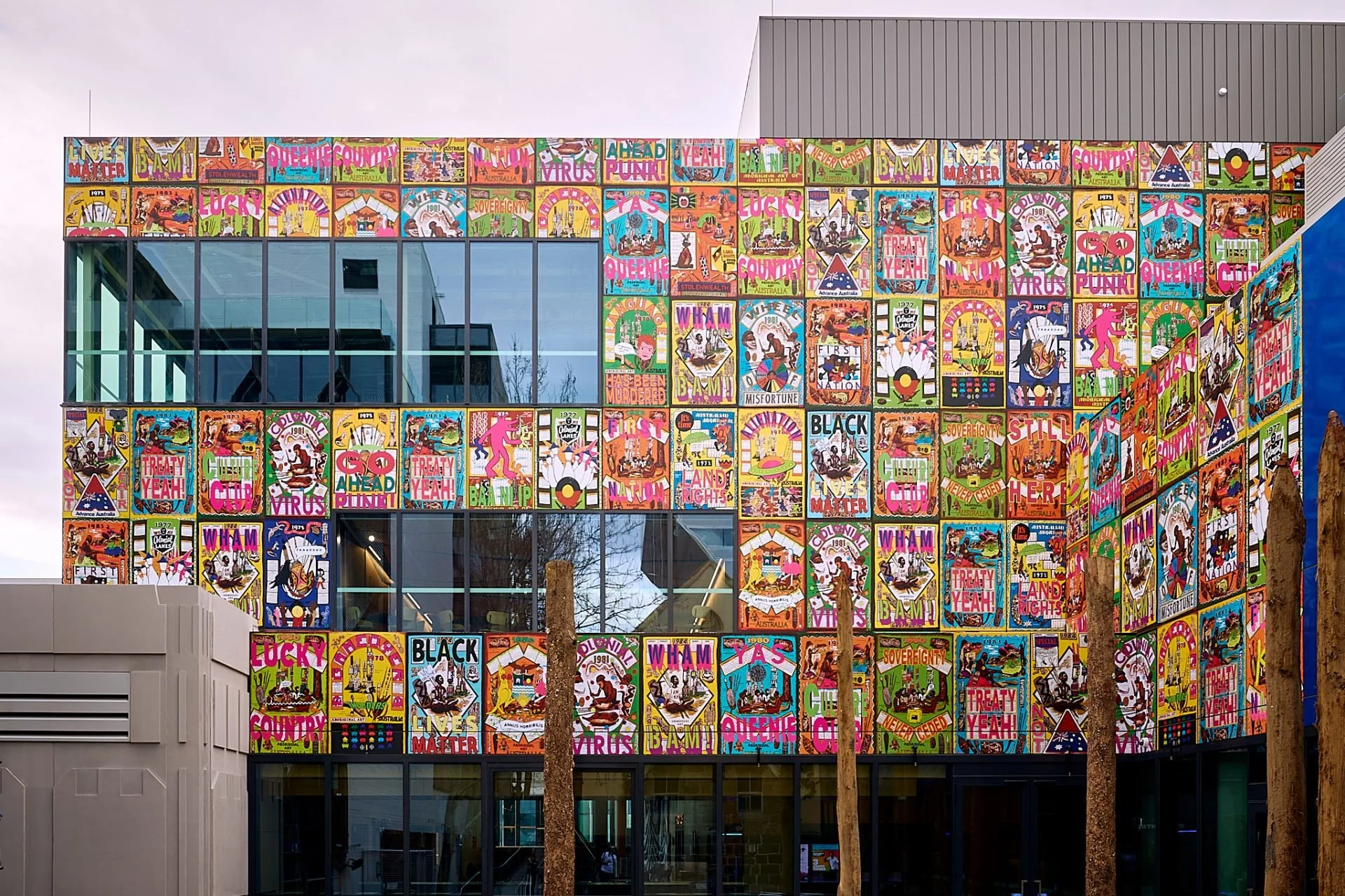 Colorful poster-covered building with large glass windows and wooden poles in front.