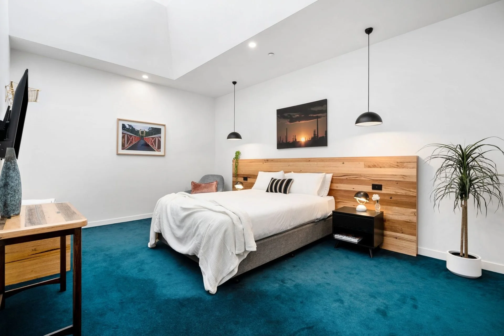 Modern hotel bedroom with a bed, nightstand, wall art, and indoor plants.