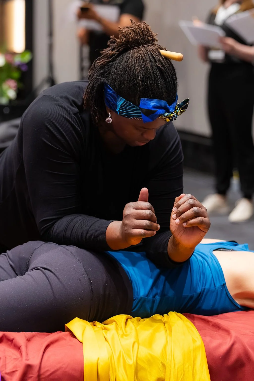 La thérapeute Khady Ngom effectuant une technique de massage thaï sur une personne couchée, lors du Sommet canadien de la massothérapie, avec d'autres personnes en arrière-plan.