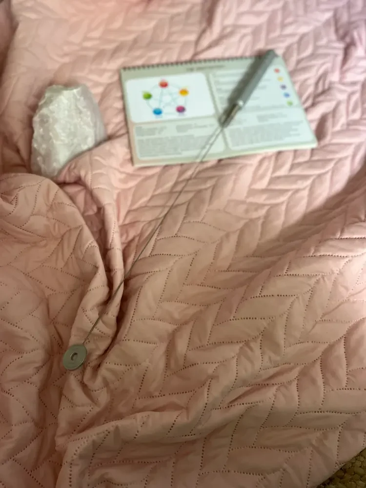 Een roze bed met een quilted dekbed, een stuk kristal en een open boek met een pen erop.