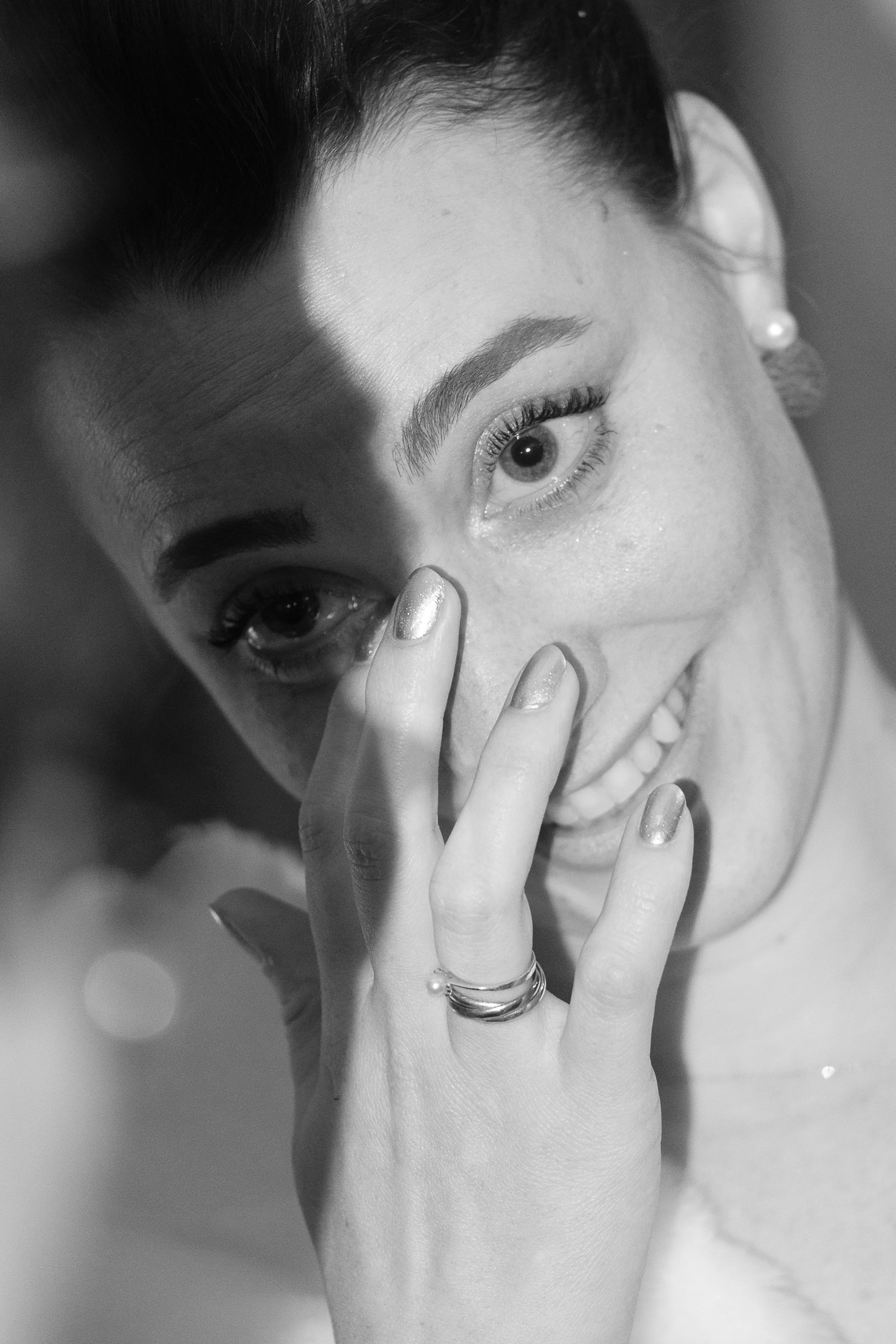 Une femme souriante avec des yeux grands ouverts, tenant sa main près de son visage, dans une photo en noir et blanc.