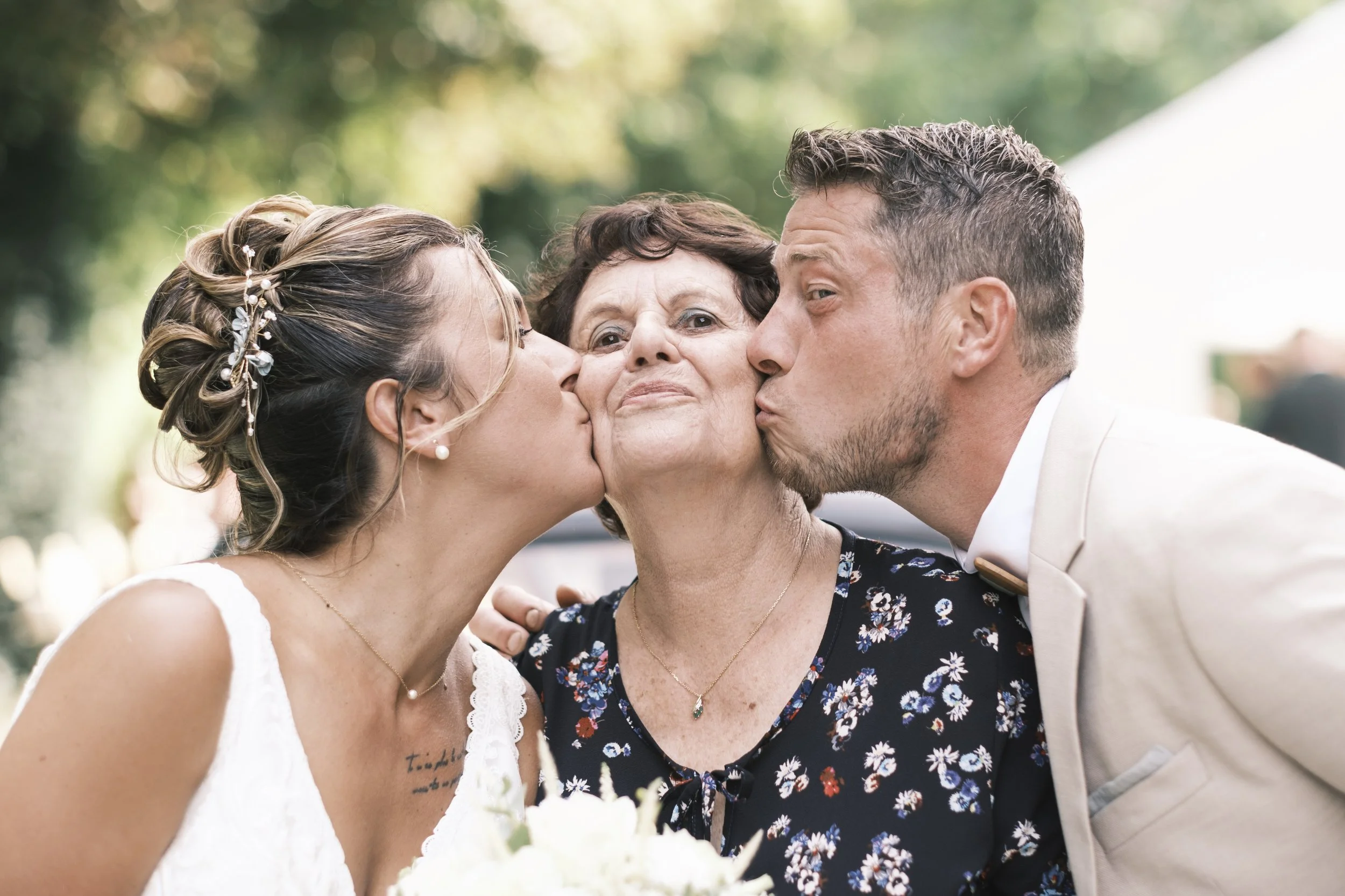 Une femme et un homme embrassent une femme plus âgée lors d'un mariage, le tout en extérieur.